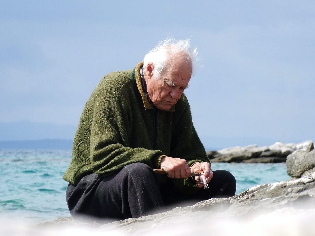 shallow focus photo of man in green long-sleeved shirt sitting near body of water