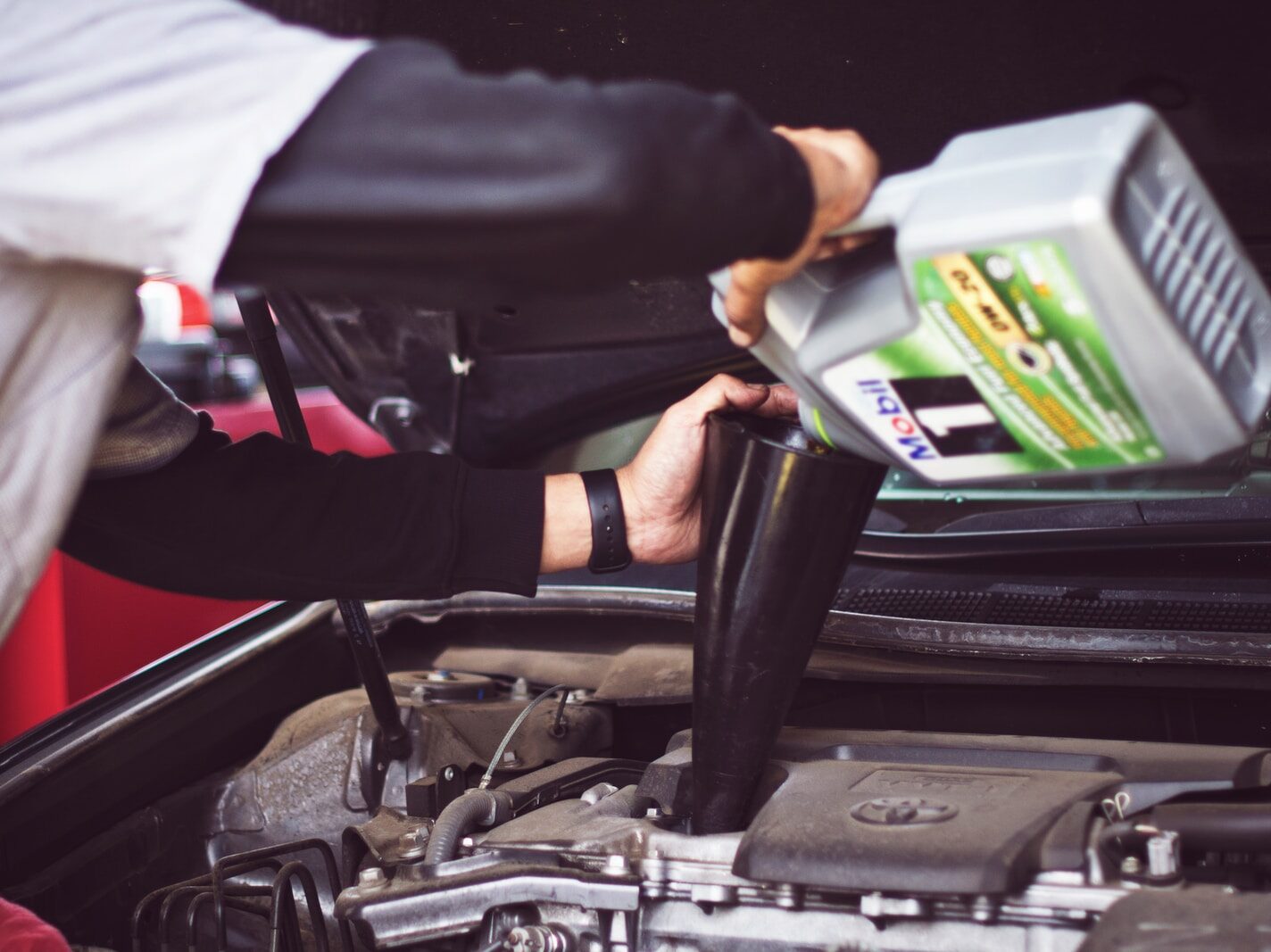 man refilling motor oil on car engine bay