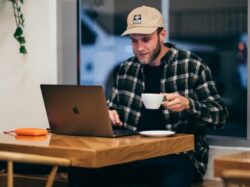 man sitting while having coffee and using laptop
