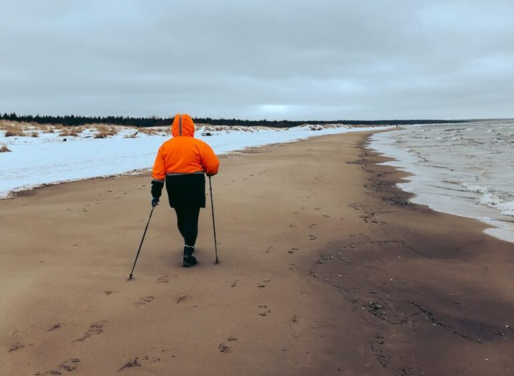 A Person in Orange Jacket and Black Pants Walking on Beach