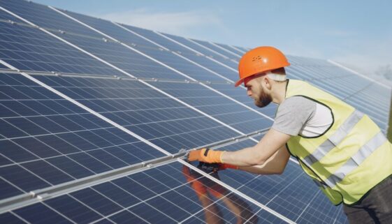 Side view of focused young man in uniform and hardhat checking setup of solar panels