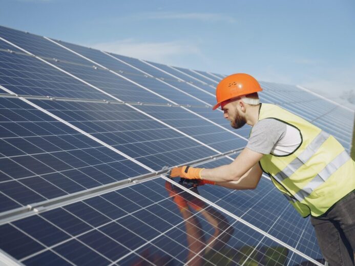 Side view of focused young man in uniform and hardhat checking setup of solar panels