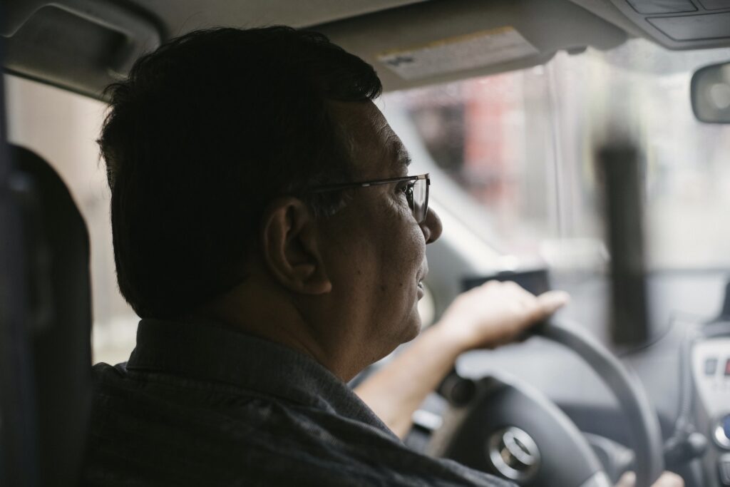 Side view of focused aged male with glasses driving automobile on street on urban background in soft daylight