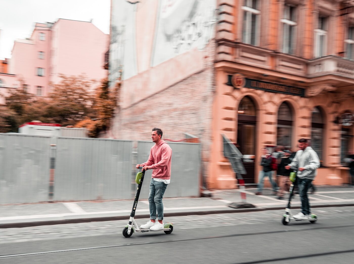 two men riding kick scooters during daytime