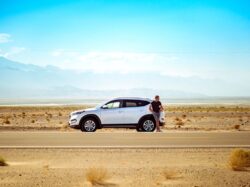 man standing beside white SUV near concrete road under blue sky at daytime