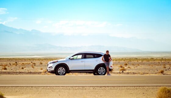 man standing beside white SUV near concrete road under blue sky at daytime