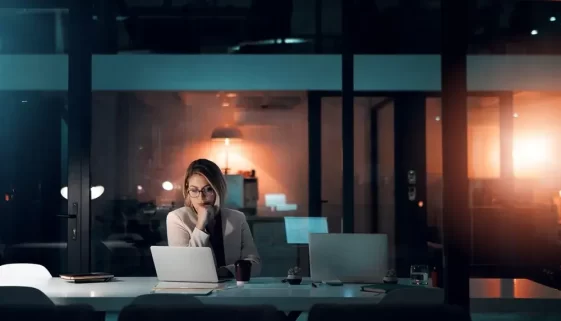 Žena sedící u počítače, večer v kanceláři.