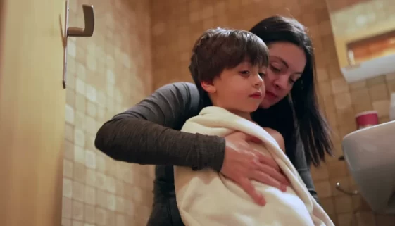 žena balí syna do ručníku v koupelně protože je zima