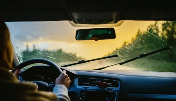 Žena řídící auto stírající přední sklo.