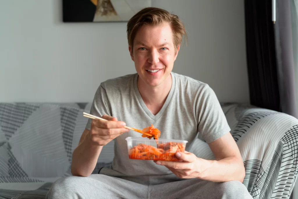 Muž sedí na gaučí a jí kimchi.
