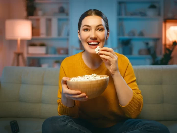 žena se dívá na televizi na gauči a sleduje popcorn
