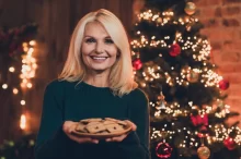 usmívající se sympatická blond žena s talířem perníčků před vánočním stromečkem