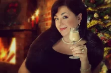 zralá atraktivní žena s číší vaječného likéru před stromečkem