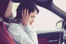 Žena za volantem zakrývající si uši proti hluku.