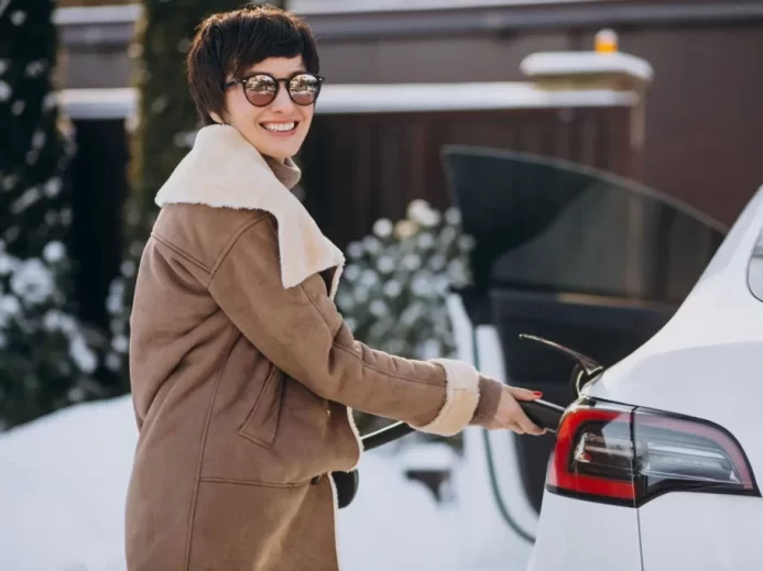 Žena nabíjející elektromobil v zimě.