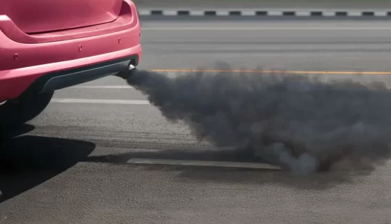 Pohled na zadní část osobního automobilu vypouštějící tmavý kouř z výfuku