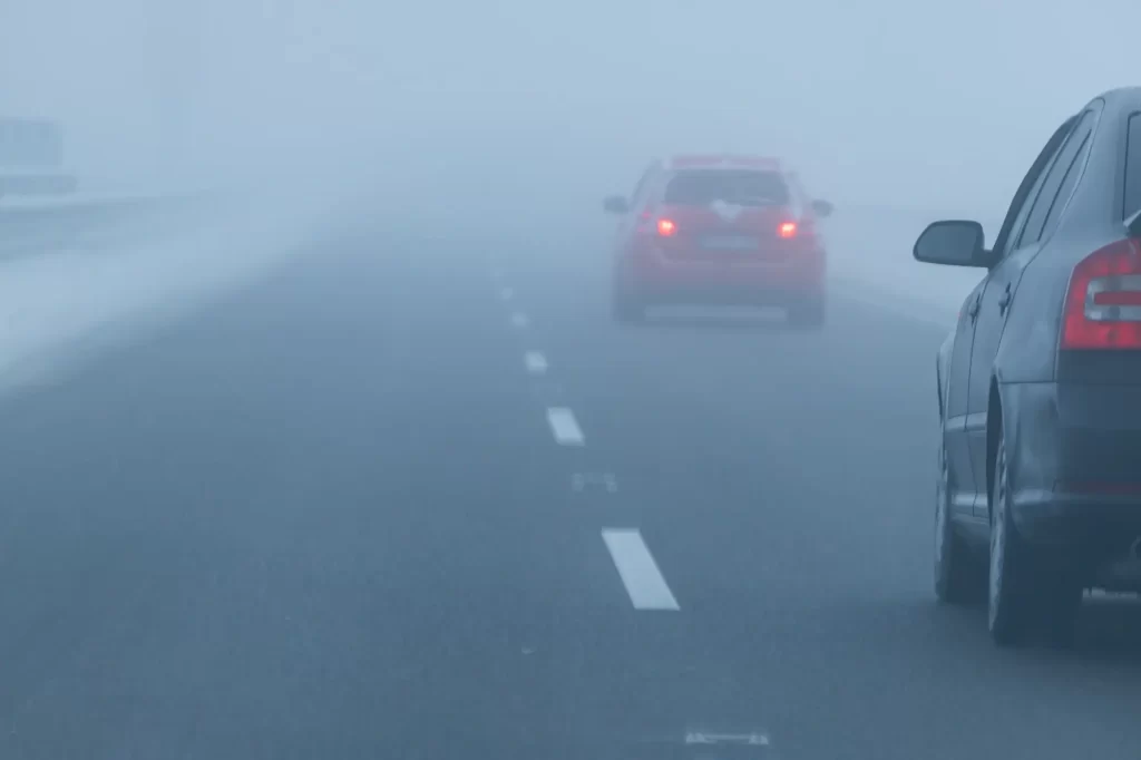 Černé auto na mlhavé zimní dálnici, v popředí před ním je červené auto