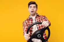 Mladý muž, držící volant na žlutém pozadí