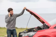 Muž volá asistenční službu, stojí u porouchaného automobilu s otevřenou kapotou