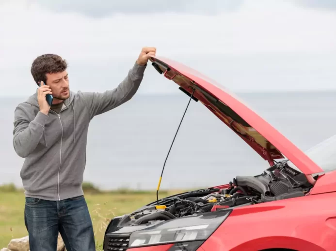 Muž volá asistenční službu, stojí u porouchaného automobilu s otevřenou kapotou
