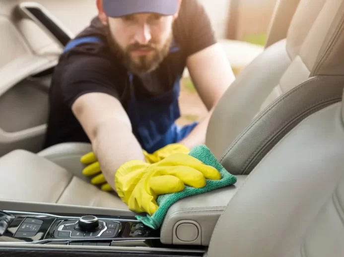 Muž se žlutými rukavicemi čistí interiér auta
