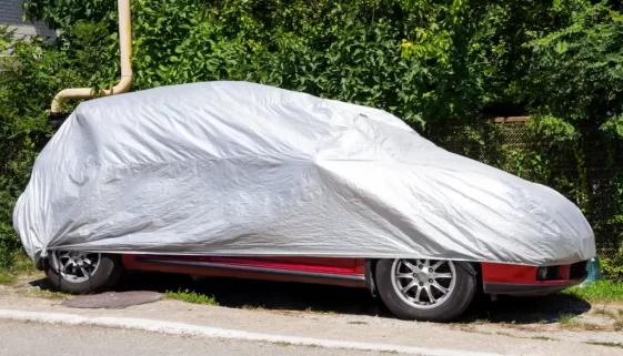 Auto stojí na kraji silnice pod ochrannou plachtou