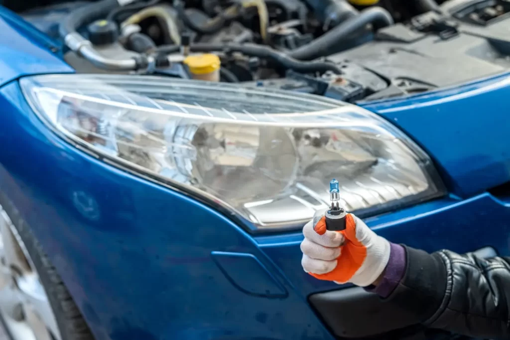 Řidič drží novou autožárovku před světlometem modrého vozu 