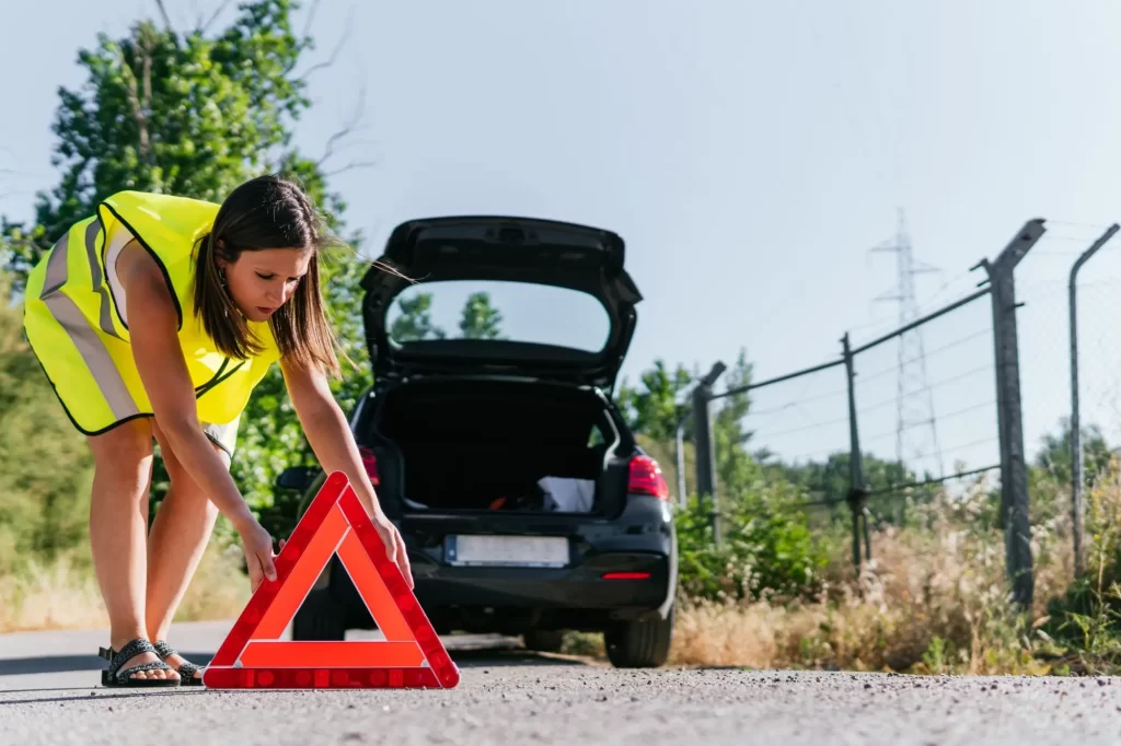 Po opuštění auta si oblečte reflexní vestu a rozložte výstražný trojúhelník, Foto: Shutterstock - MotorGuru.cz Mladá žena v reflexní vestě rozkládá výstražný trojúhelník za autem
