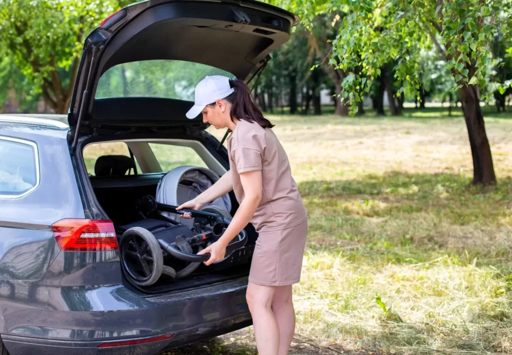 Žena vkládá složený dětský kočárek do kufru auta