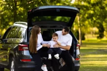 Maminka a tatínek sedí s malým chlapcem v otevřeném kufru SUV