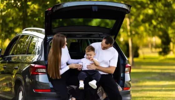 Maminka a tatínek sedí s malým chlapcem v otevřeném kufru SUV
