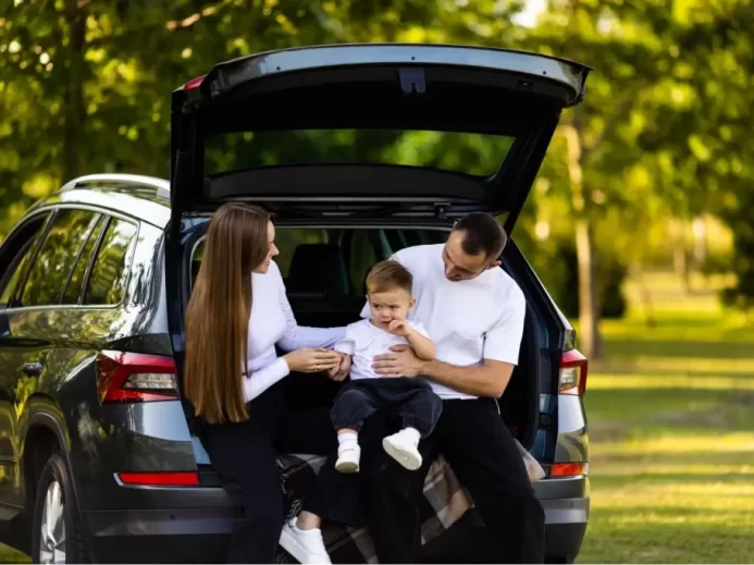 Maminka a tatínek sedí s malým chlapcem v otevřeném kufru SUV