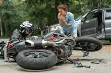 Motorkář po nehodě sedí u své motorky, zatímco žena reaguje na situaci