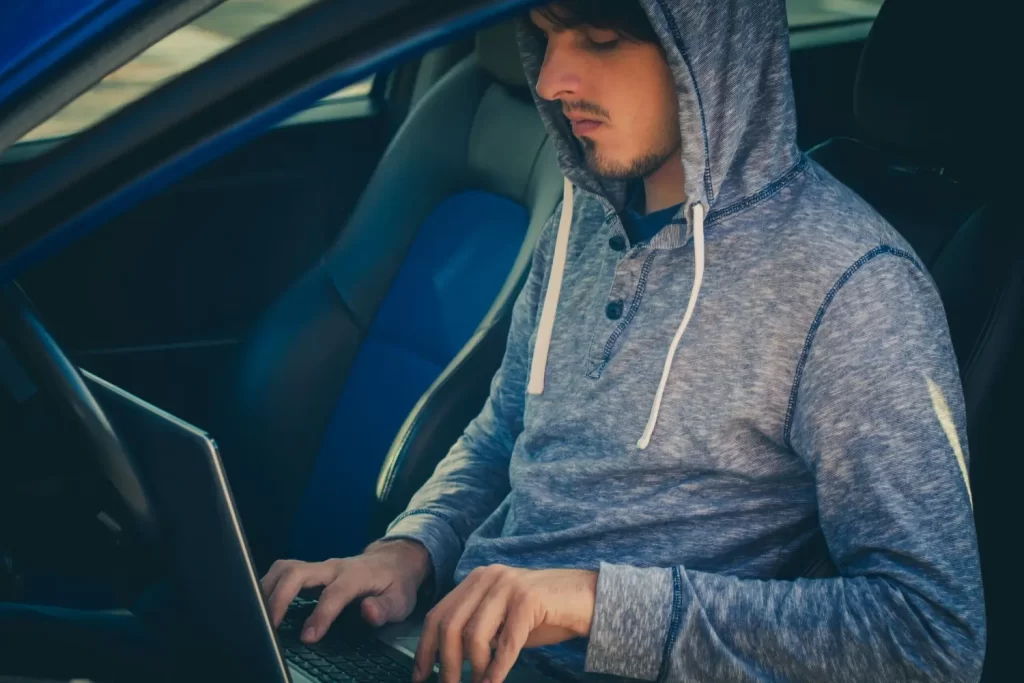 Muž v mikině sedí v autě s notebookem