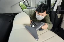 Muž s respirátorem čistí autosedačku vysavačem