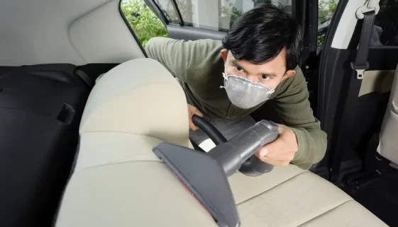 Muž s respirátorem čistí autosedačku vysavačem