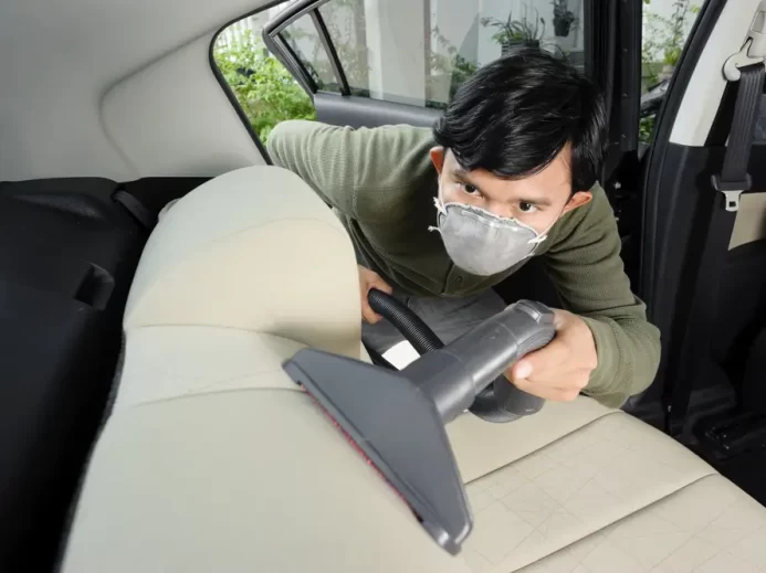 Muž s respirátorem čistí autosedačku vysavačem