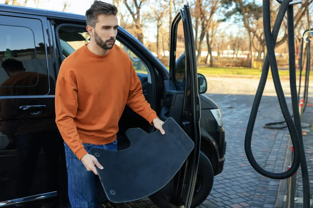 Muž u benzínové pumpy vyndává z auta autokoberec.