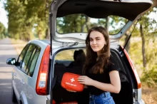 Mladá žena drží lékárničku u otevřeného kufru auta