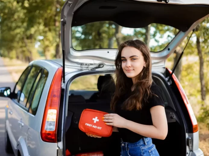 Mladá žena drží lékárničku u otevřeného kufru auta