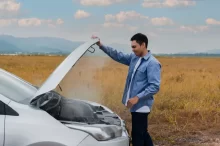 Muž stojí u otevřené kapoty auta, ze které se kouří