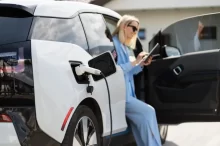 Žena v modrém nabíjí bílý elektromobil