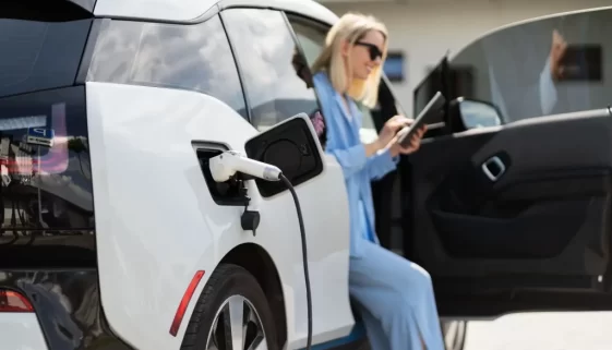 Žena v modrém nabíjí bílý elektromobil