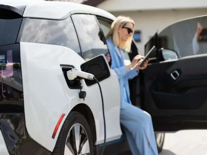 Žena v modrém nabíjí bílý elektromobil