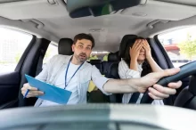 Žena si při řízení auta zakrývá oči, instruktor autoškoly drží volant