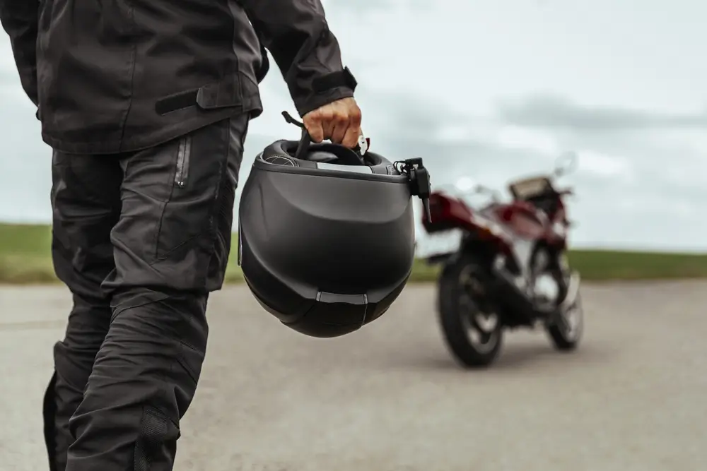 Muž kráčí ke své motorce a v rukou drží helmu. Detailní záběr na motocyklovou helmu.