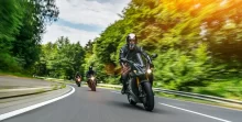Trojice motorkářů jede po silnici v lese