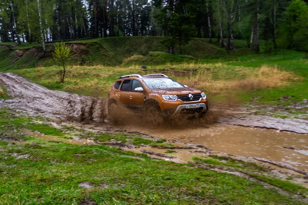 Oranžové SUV Renault projíždí vysokou rychlostí kaluží a bahnem