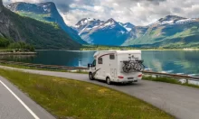 Obytný vůz parkuje u klidného fjordu obklopeného horami, s koly připevněnými na zadní straně