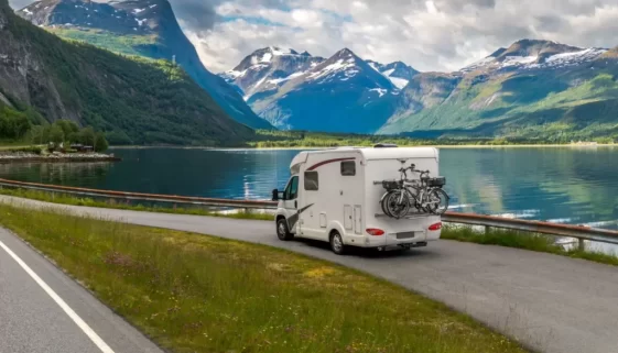 Obytný vůz parkuje u klidného fjordu obklopeného horami, s koly připevněnými na zadní straně